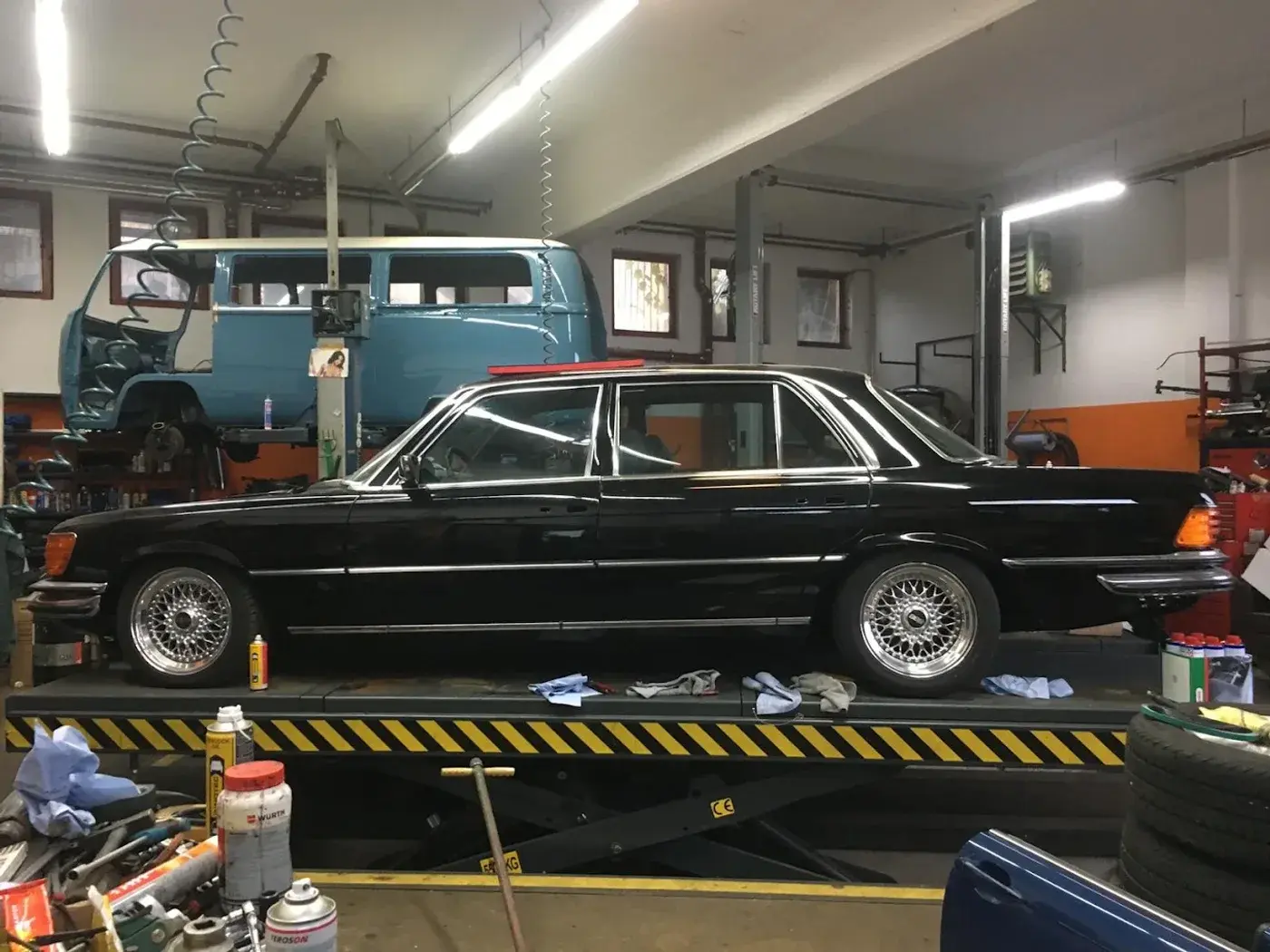 Werkstatthalle mit Mercedes-Benz Limousine auf der Hebebühne und Oldtimer-Bus im Hintergrund